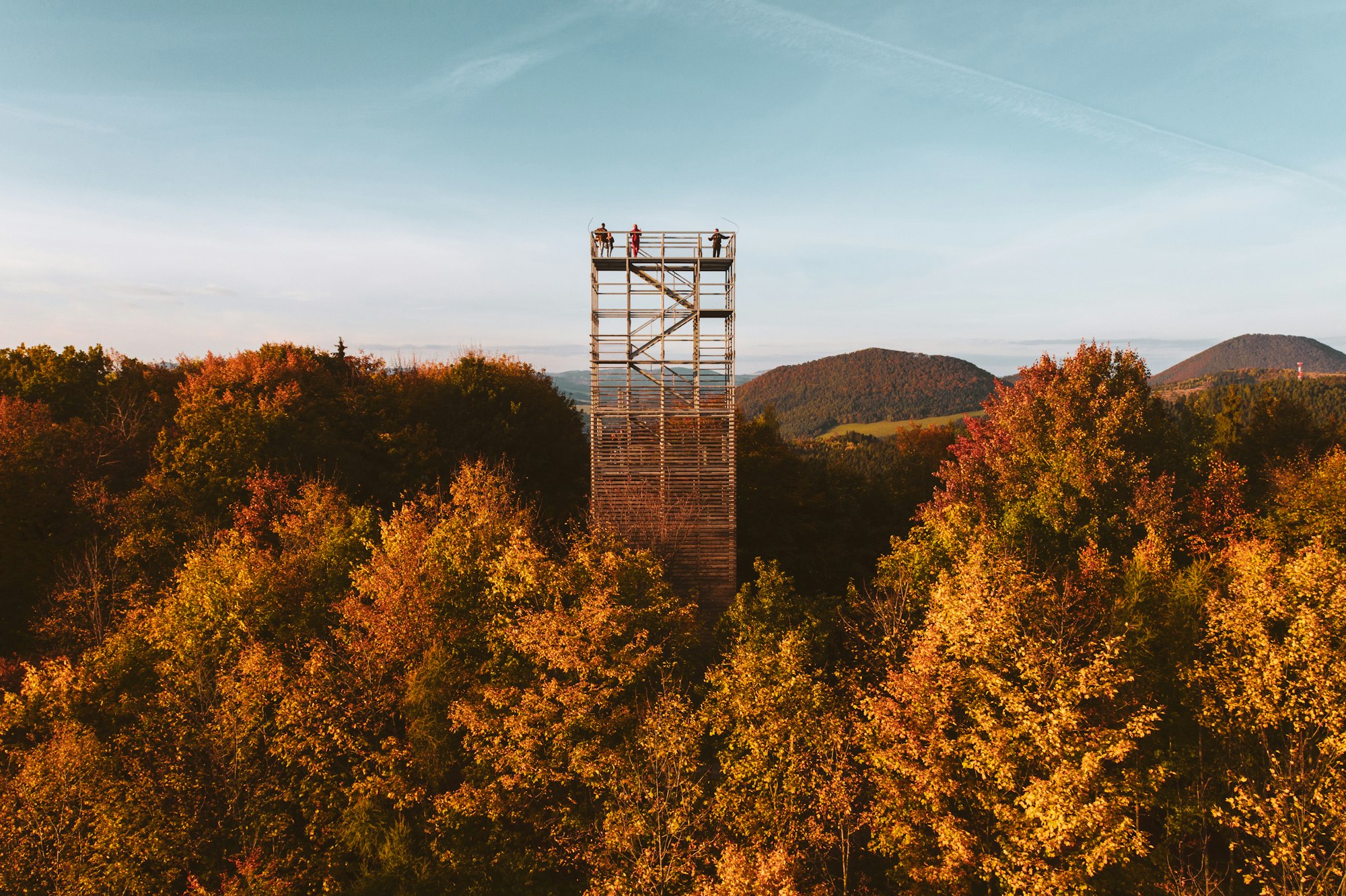 Aerial view of a wooden lookout tower in autumn nature. People stand on the observation tower